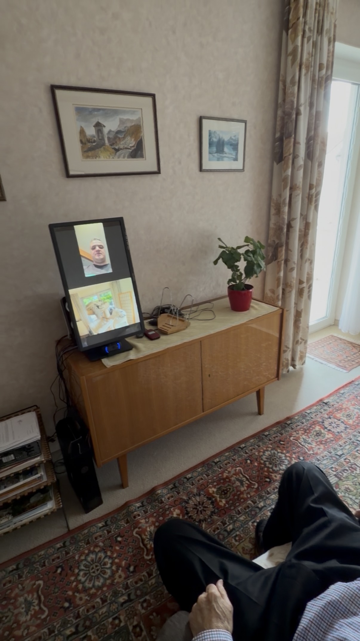 HerzTV steht im Wohnzimmer und zeigt einen Videoanruf auf dem großen Bildschirm